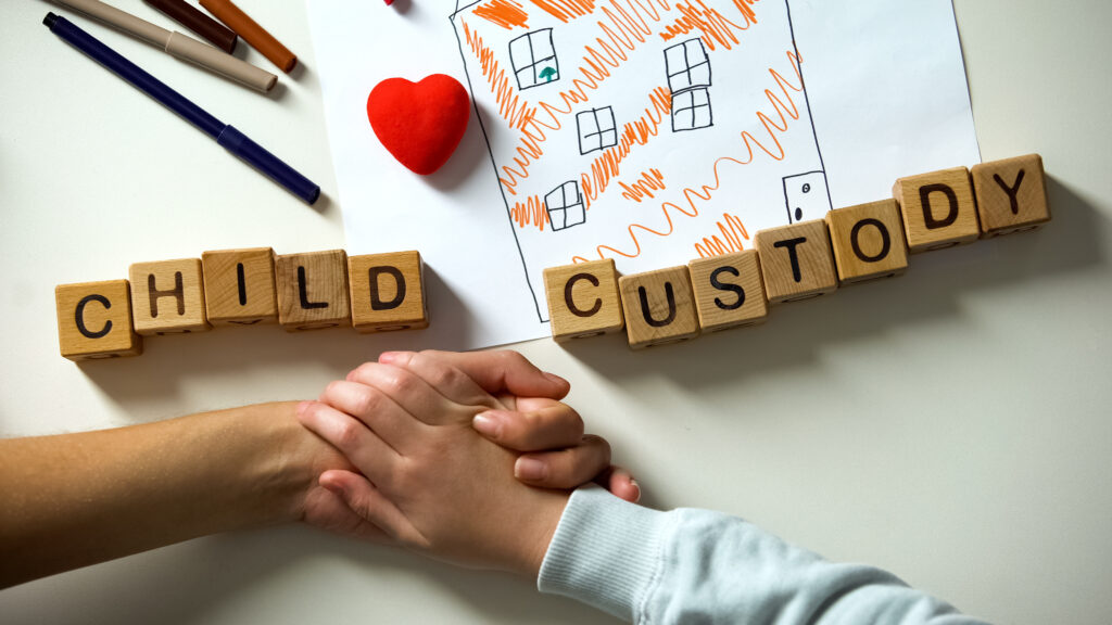 Parents holding hands over table with wood blocks spelling child custody