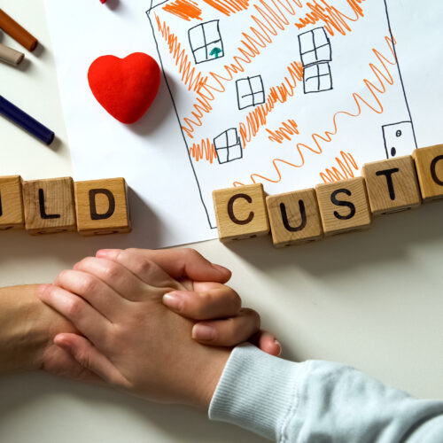 Parents holding hands over table with wood blocks spelling child custody