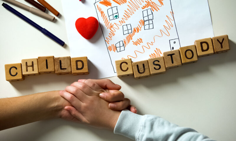 Parents holding hands over table with wood blocks spelling child custody